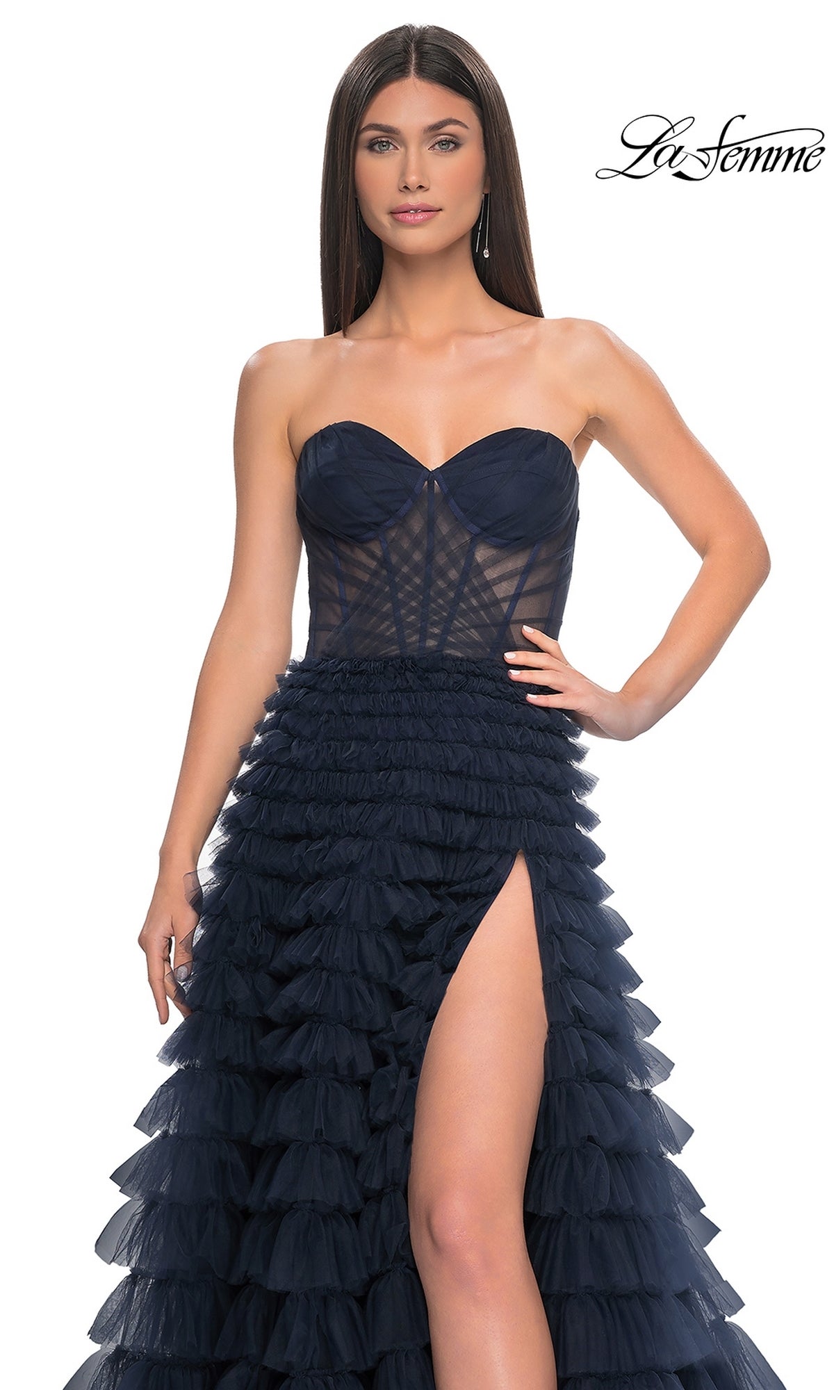 A woman wears the La Femme Strapless Long Ruffled Prom Dress 32283 in navy blue, featuring a sheer bodice, high thigh slit, and layered ruffled A-line skirt. The